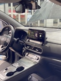 The interior of a modern car featuring a digital dashboard, infotainment system with Apple CarPlay displayed, and a steering wheel. The dashboard includes various buttons and dials, and there is a large sunroof visible overhead. The seats appear to be cloth upholstered, and there are items stored in the console.