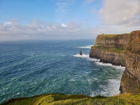 green and brown rock formation beside body of water during daytime in Cliffs of Moher Ireland