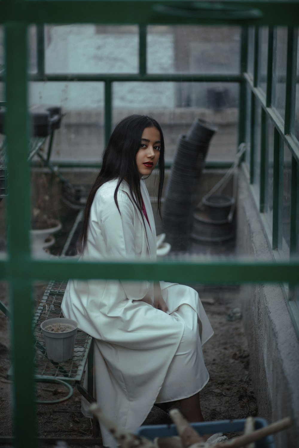 woman in white robe sitting on green metal fence during daytime