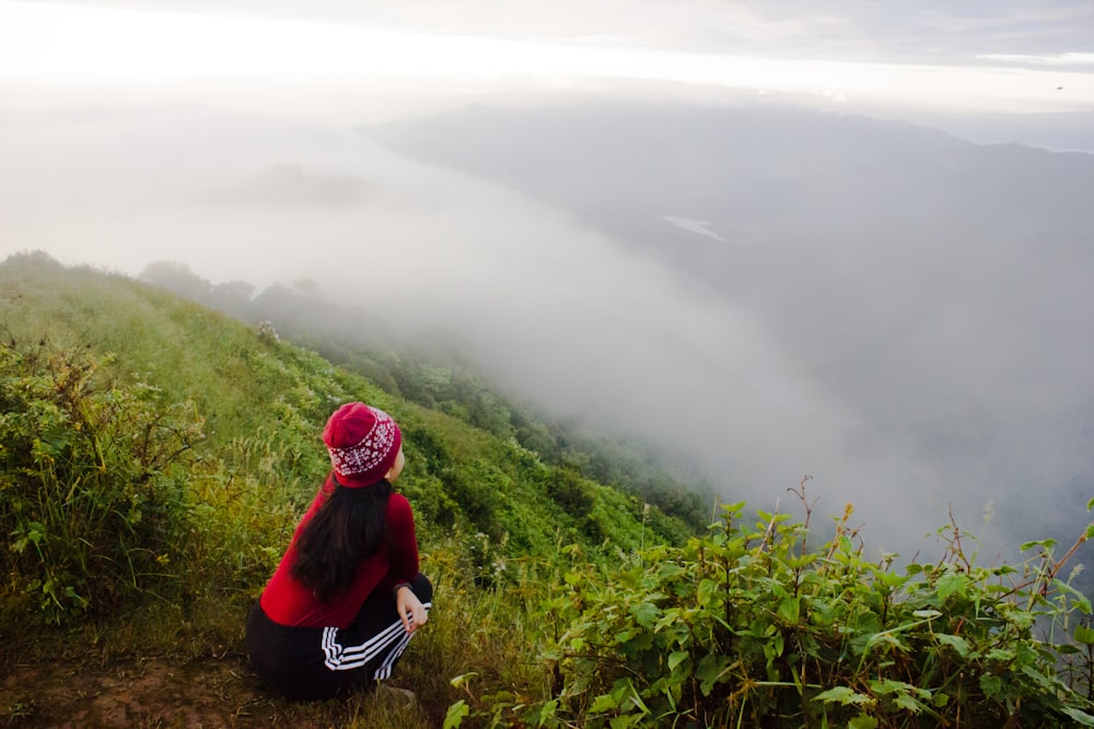 woman in red hoodie sitting on green grass field during daytime