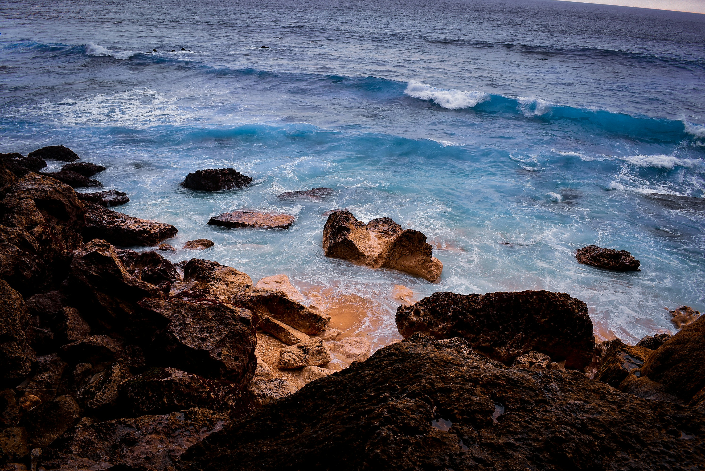 brown rocky shore with ocean waves crashing on rocks during daytime