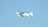 A small white aircraft with the letters 'VCA' on its side is flying mid-air against a clear blue sky. The aircraft has two wings and a propeller that is in motion.