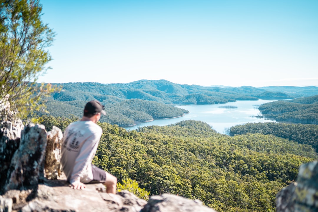 man in white dress shirt sitting on rock near green trees during daytime