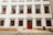 A symmetrical facade of a European academic building featuring multiple windows with red frames. The entrance has a double door, also painted red. The sign above the door indicates it is a faculty of a university. The building is constructed with smooth white walls and trimmed with stone accents. Stone steps lead to the entrance.