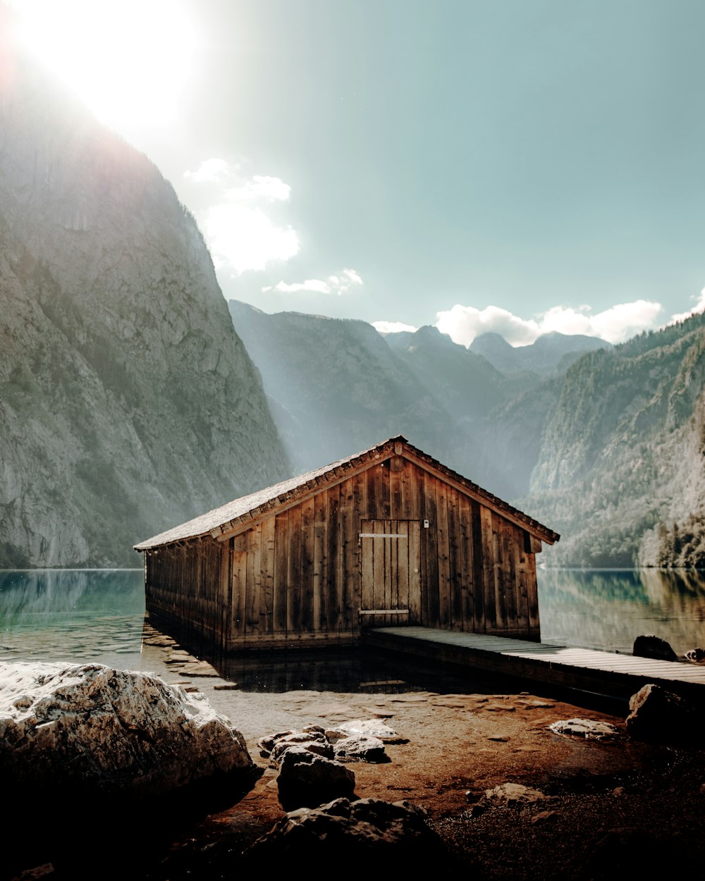 brown wooden house near lake and mountain during daytime