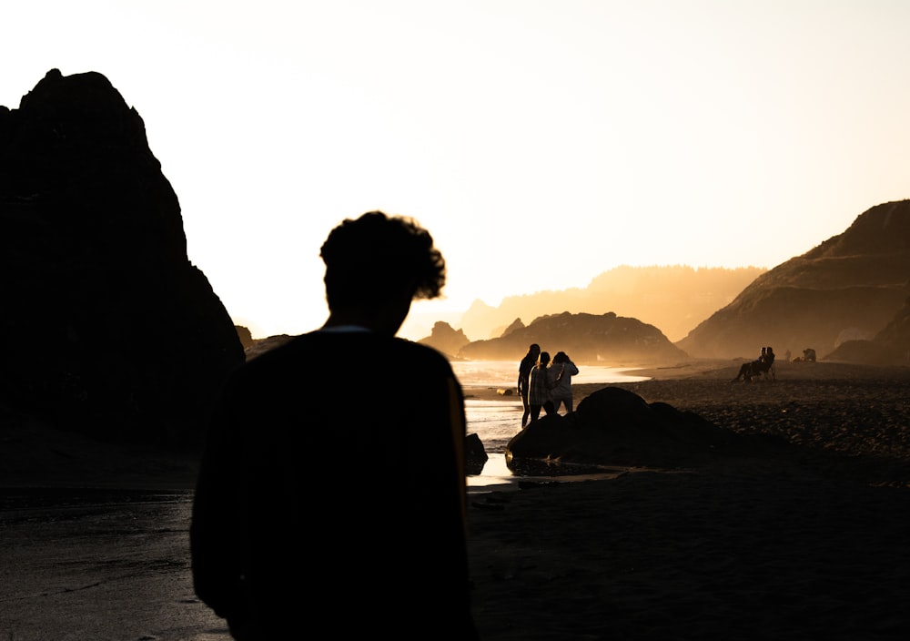 silhouette of man and woman sitting on rock near body of water during daytime