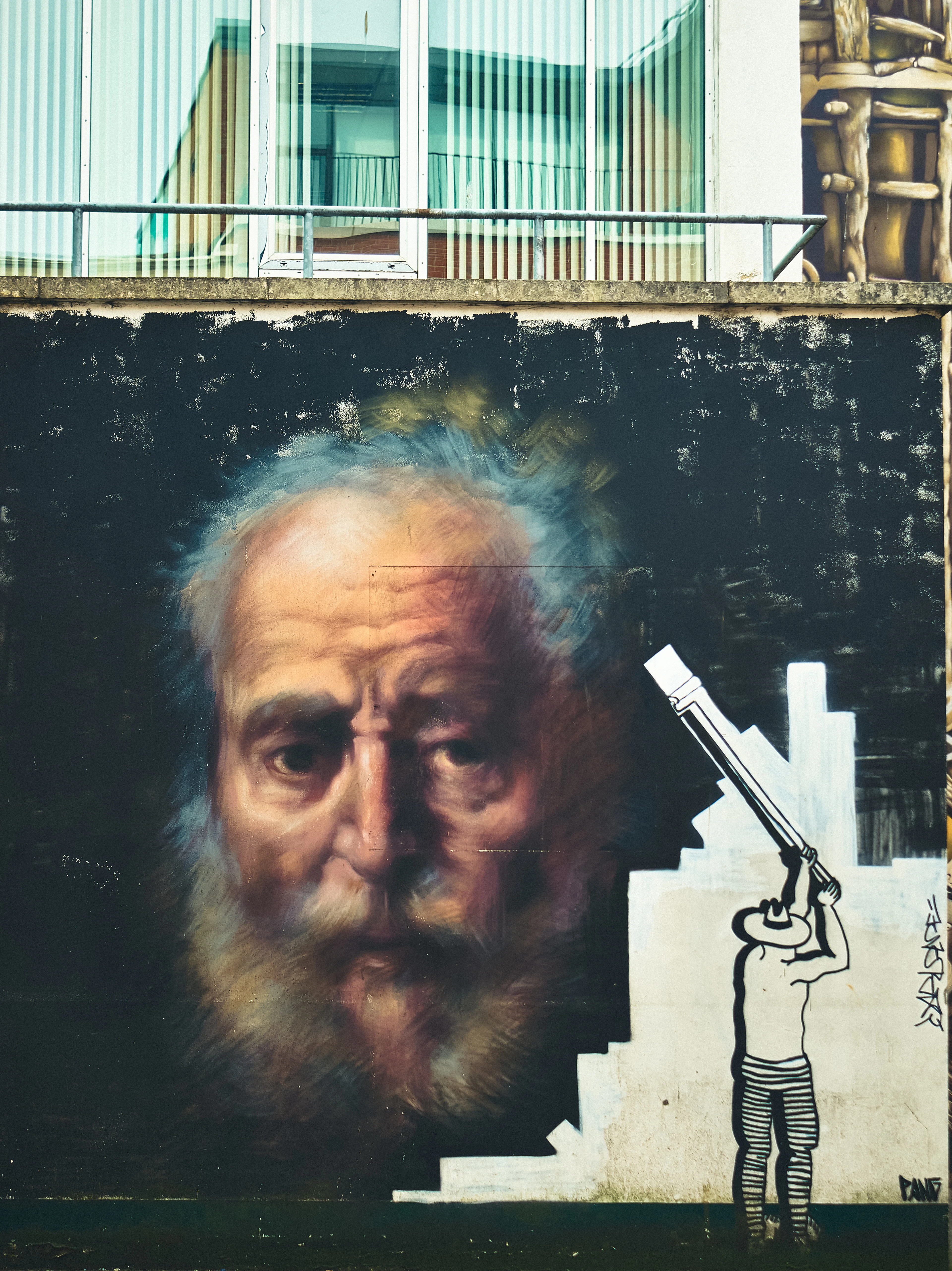 A street art mural in Belfast's Cathedral Quarter showing a bearded man's face beside a figure with a telescope.
