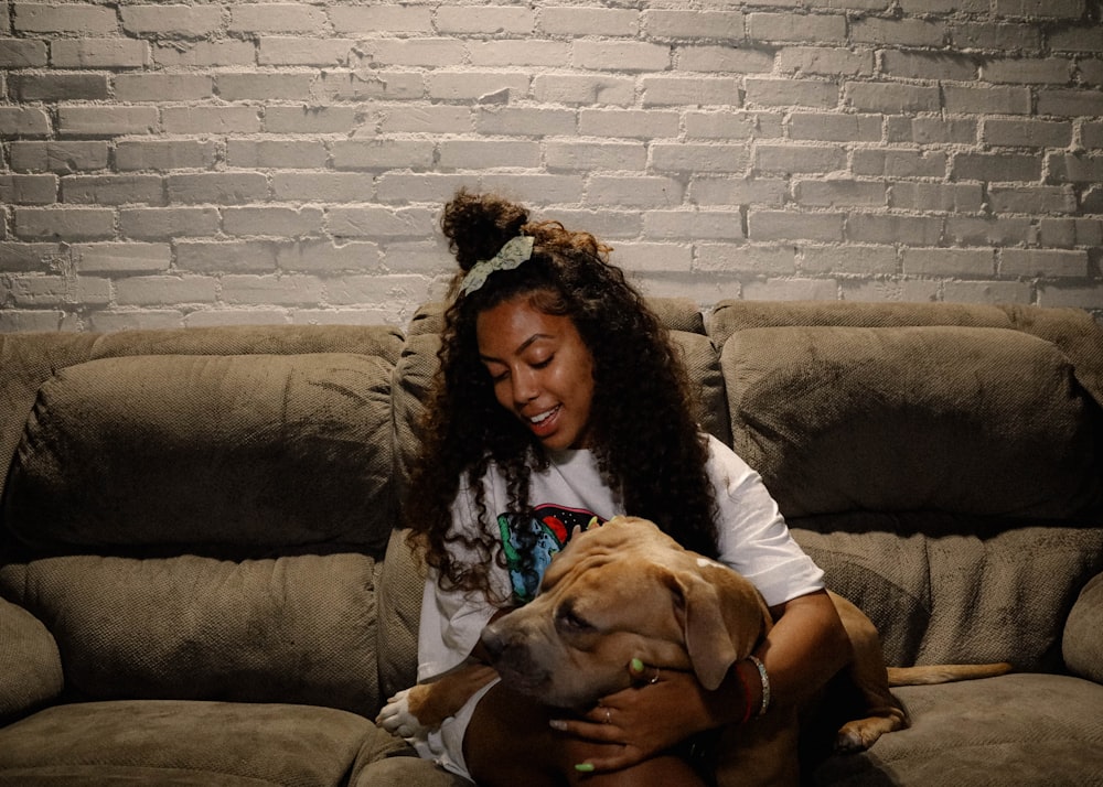 woman in black shirt sitting on brown couch beside brown short coated dog