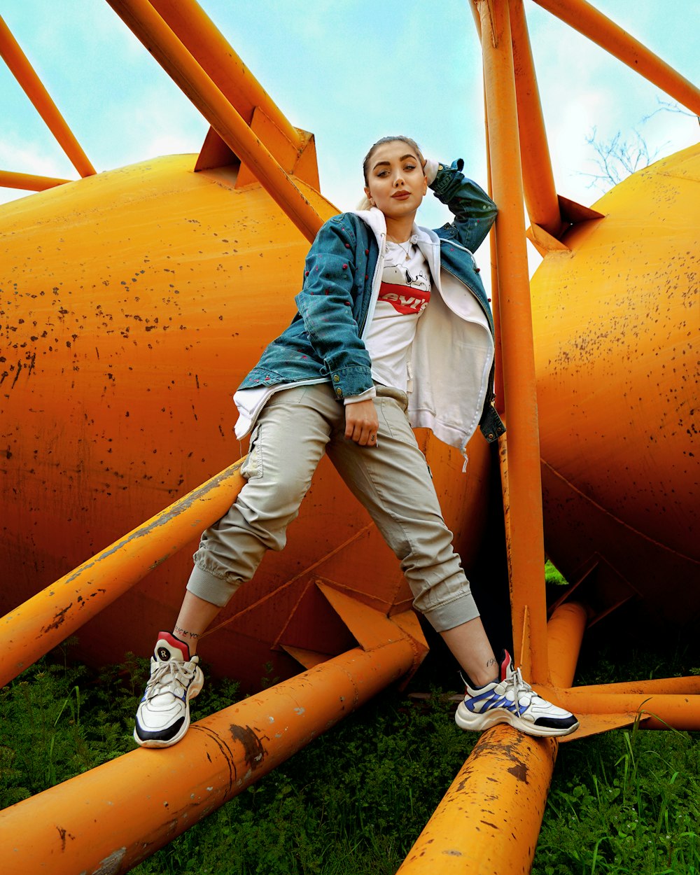 girl in blue denim jacket and blue denim jeans standing on orange metal pipe during daytime