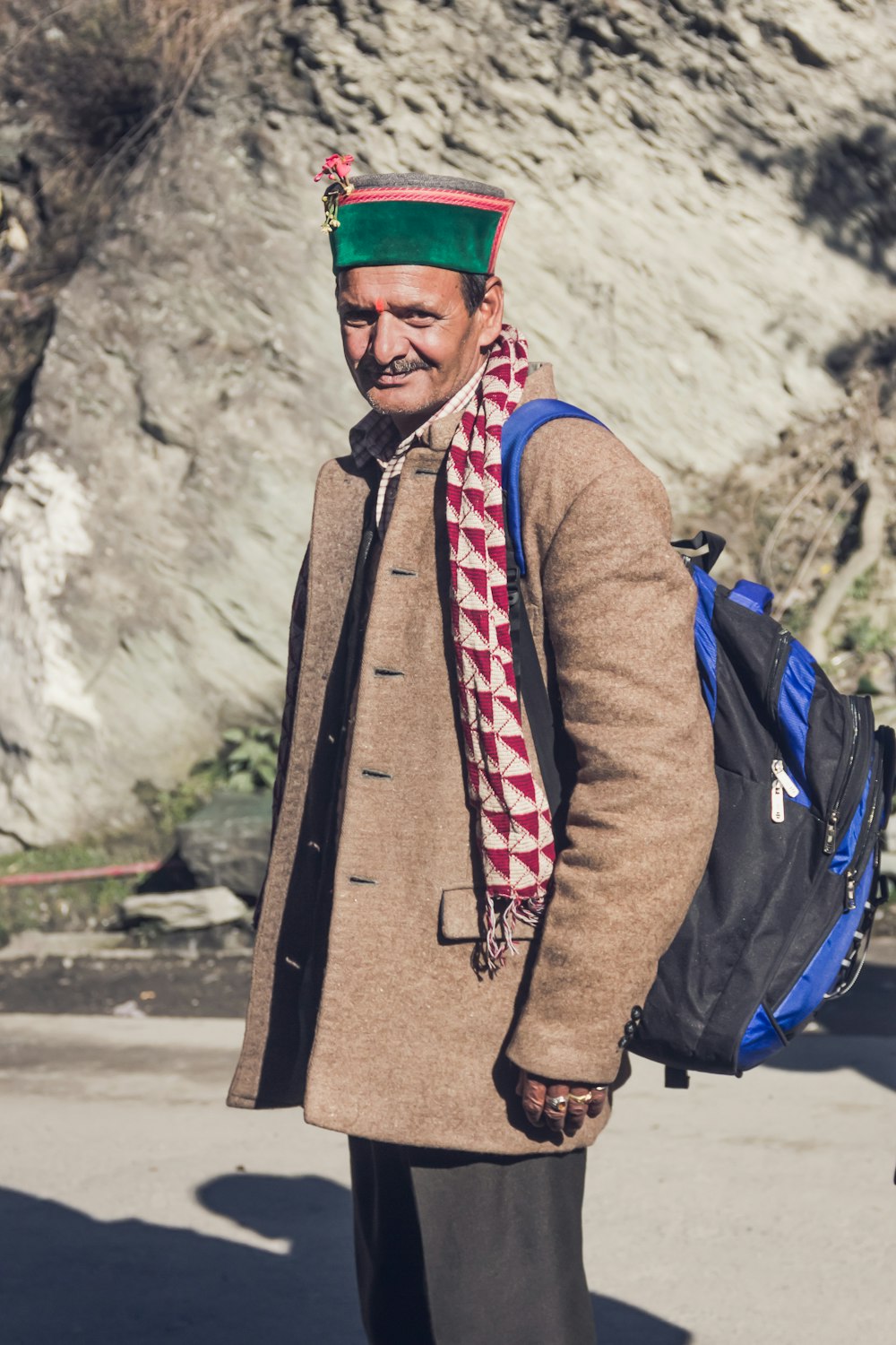 man in brown coat and blue backpack standing near brown rock