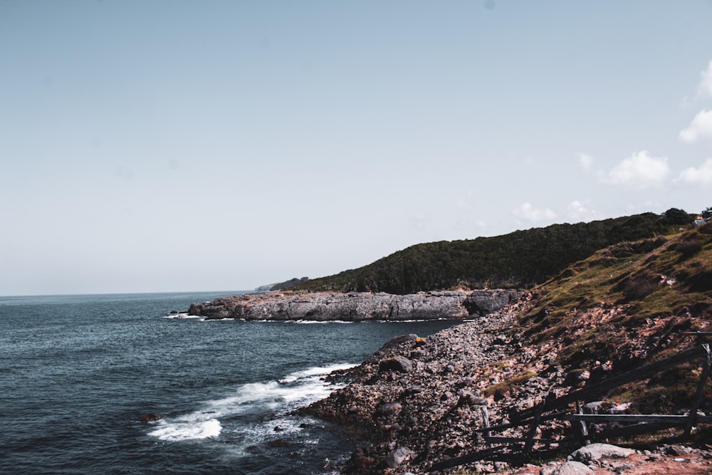 green and brown mountain beside sea under blue sky during daytime