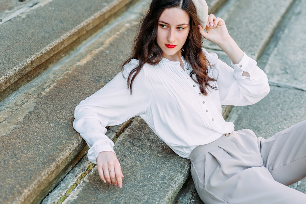 woman in white dress shirt and gray pants sitting on gray concrete stairs