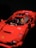 A red toy car resembling a sports car with a figure inside, featuring a yellow face and a helmet. The toy has intricate details, including side mirrors and an interior dashboard.