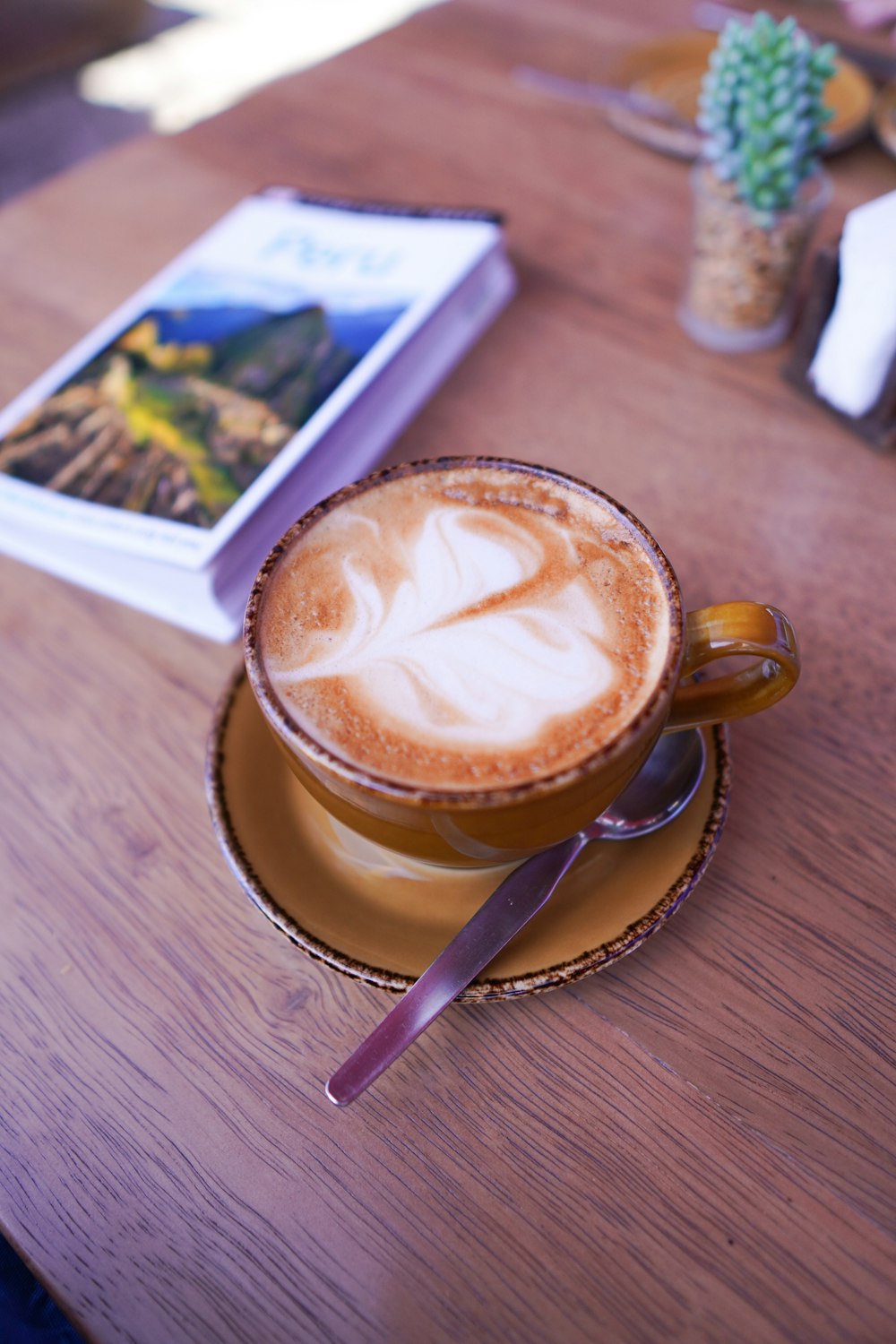 Cappuccino in brauner Keramiktasse mit silbernem Löffel auf braunem Holztisch