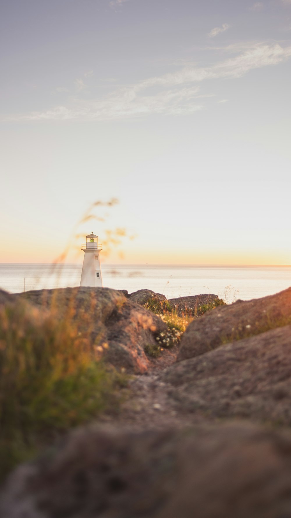 farol branco no topo da colina perto do corpo de água durante o dia