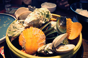 Assorted shellfish including clams and mussels arranged on a wooden tray.