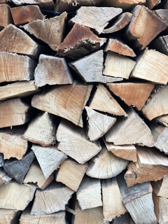 A neatly stacked pile of chopped firewood with visible grain and texture on each piece of wood. The logs are cut into triangular shapes and are arranged in a closely packed manner.