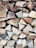 A neatly stacked pile of chopped firewood with visible grain and texture on each piece of wood. The logs are cut into triangular shapes and are arranged in a closely packed manner.