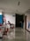 A hallway with tables and chairs, featuring a person sitting at a table using a laptop. The chairs are red and stylish, and there are accessibility signs on the wall. Another person walks towards a dimly lit area holding something in their hand.
