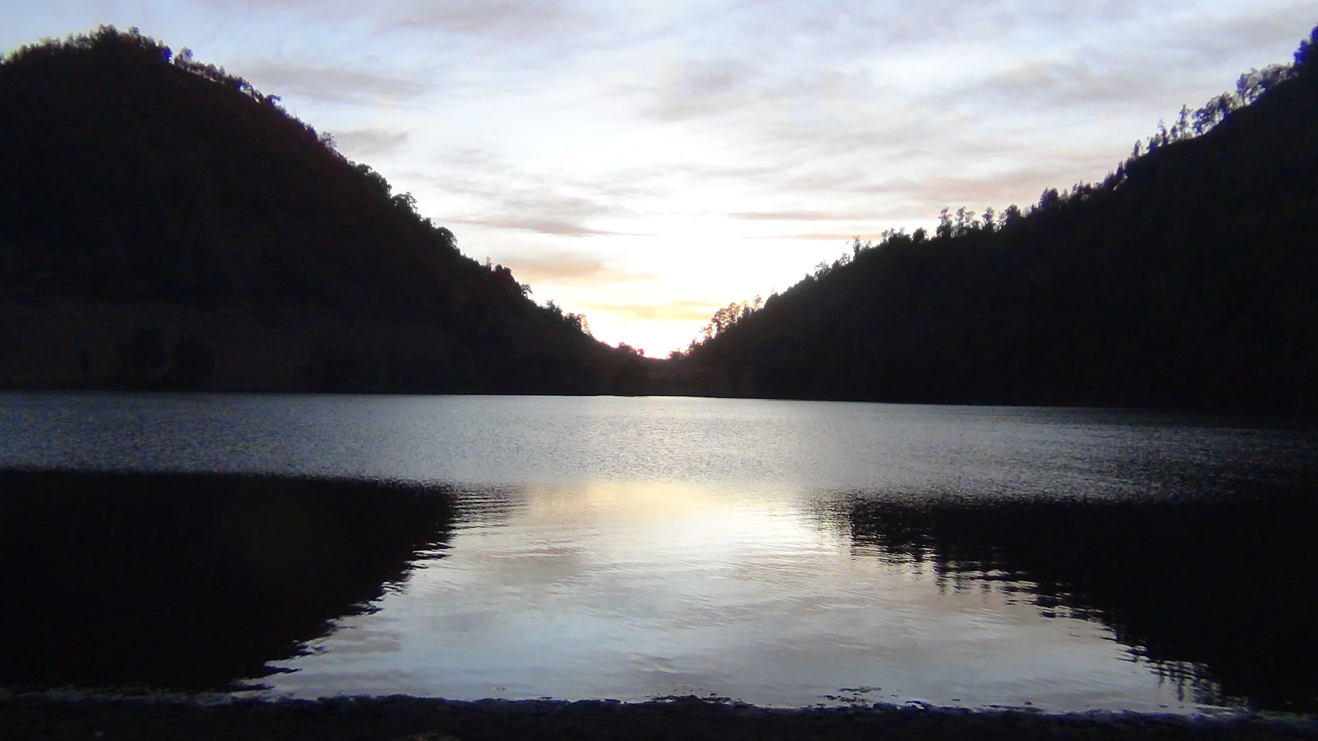 A serene landscape at dawn with soft pastel skies and a calm lake reflecting the colors.