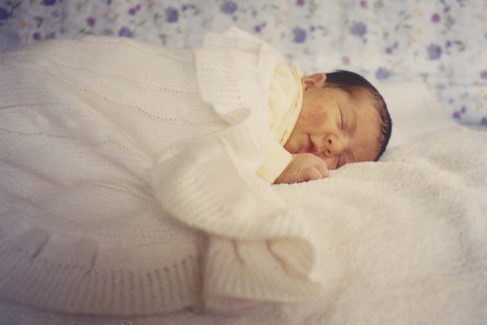 Baby im weißen Langarmshirt auf weißem Textil liegend