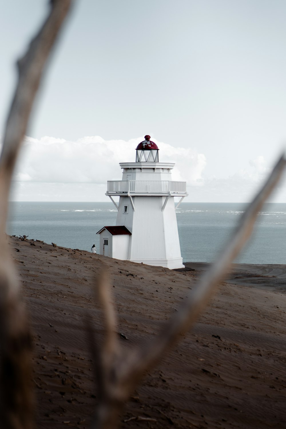 white and red lighthouse on brown sand near body of water during daytime