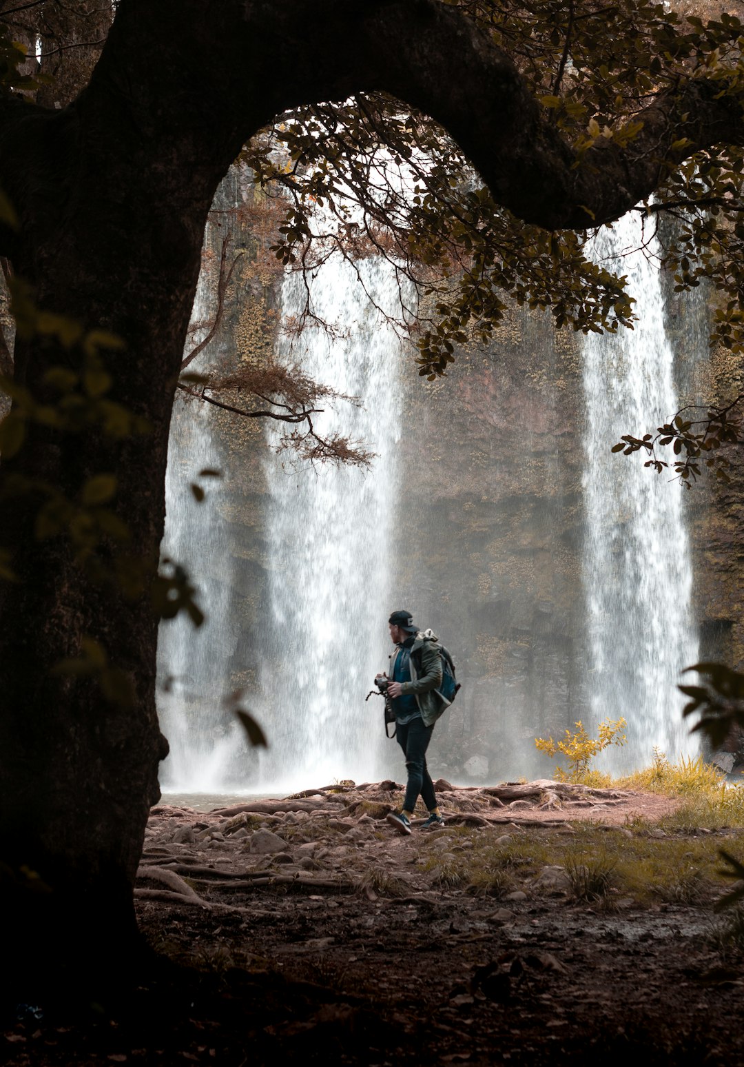 man in black jacket and blue denim jeans standing near waterfalls during daytime