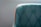 A teal upholstered chair with a quilted pattern and button detailing is highlighted by a bright orange trim. The focus is on the left section of the chair, with a soft gray background enhancing the elegant design.
