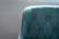 A teal upholstered chair with a quilted pattern and button detailing is highlighted by a bright orange trim. The focus is on the left section of the chair, with a soft gray background enhancing the elegant design.