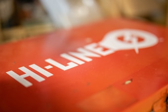 A red surface features bold white text that reads 'HI-LINE' alongside a stylized light bulb graphic with a power symbol. The background is blurred, drawing focus to the text and design.
