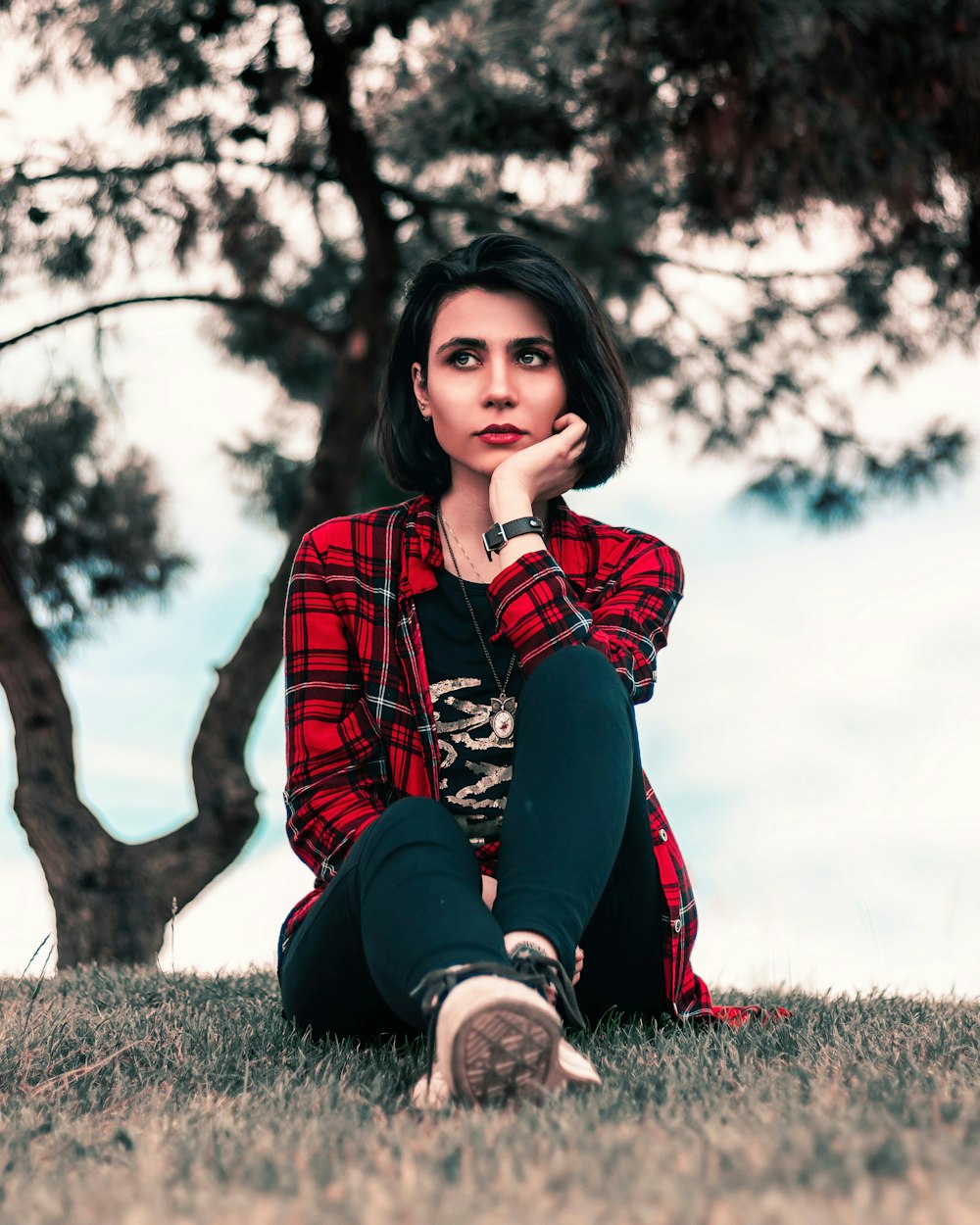 woman in red and black plaid dress shirt and black pants sitting on grass field