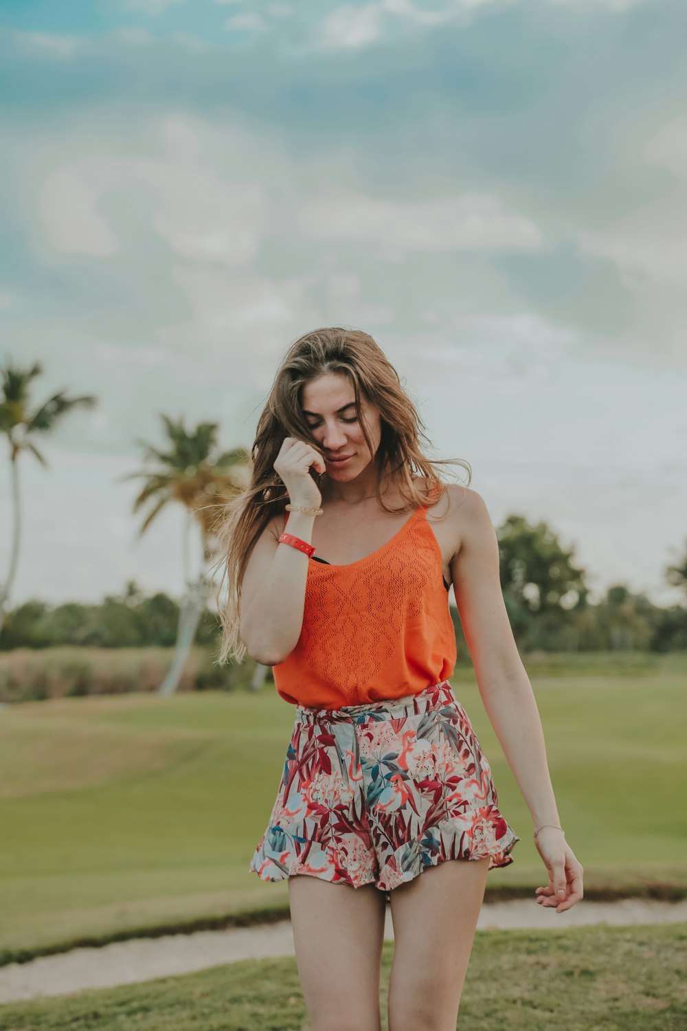 woman in red tank top and white floral skirt standing on green grass field during daytime