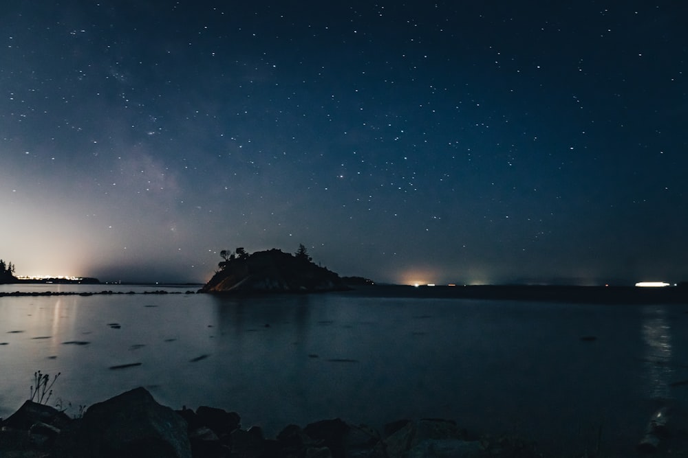 silhouette of rock formation on body of water during night time