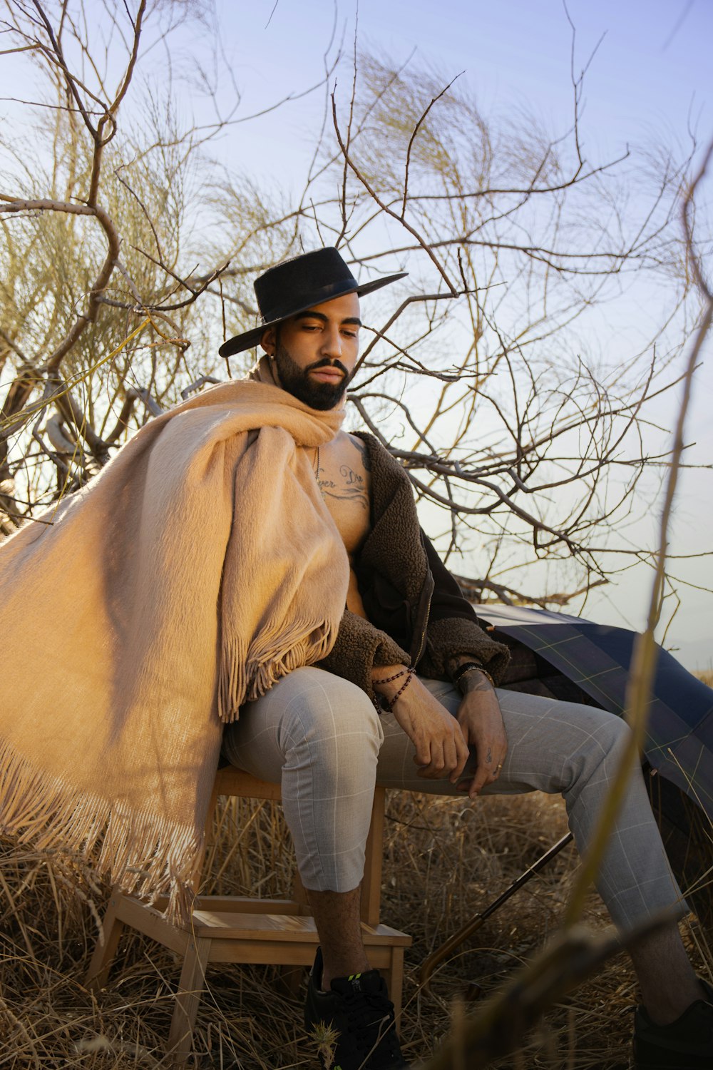 woman in black hat and brown scarf sitting on brown dried grass during daytime