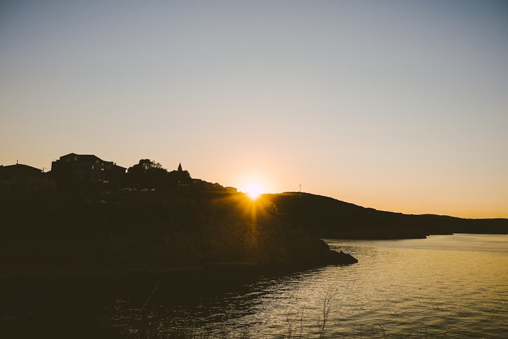 silhouette of mountain beside body of water during sunset