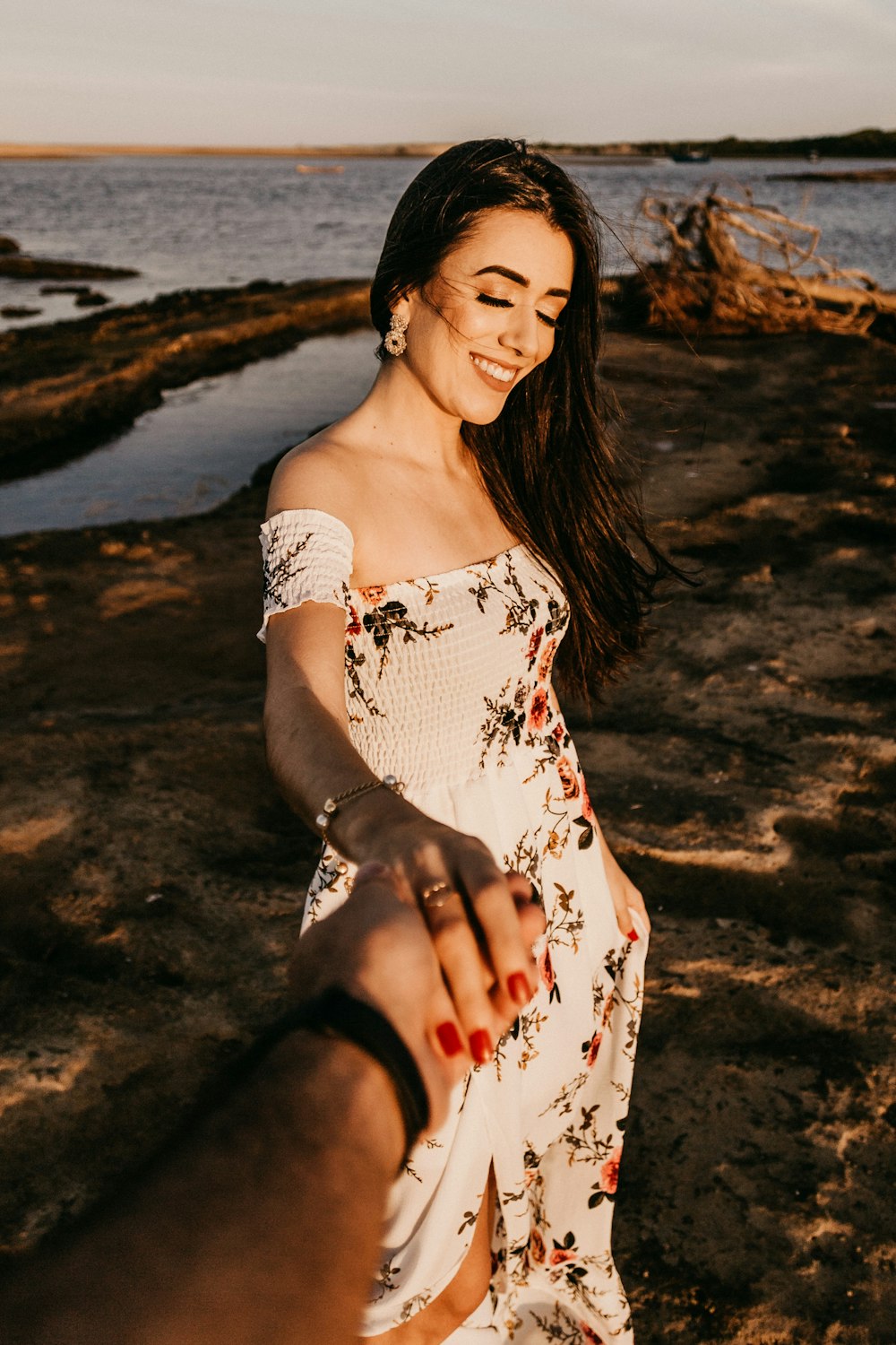 woman in white and red floral spaghetti strap dress standing on beach shore during daytime