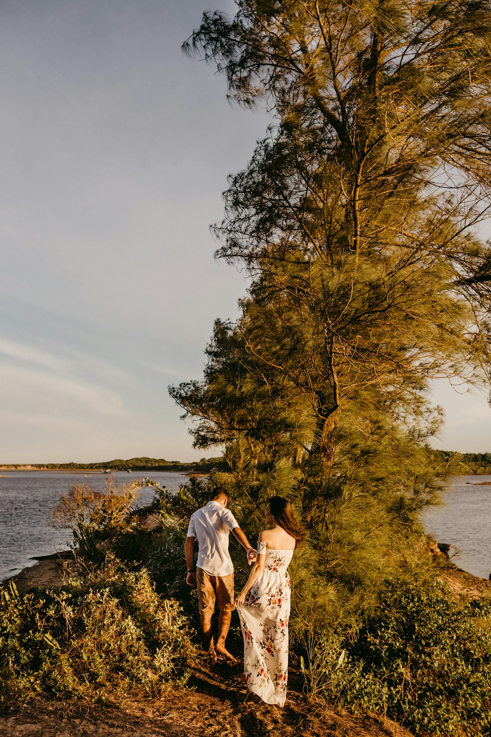 couple standing on green grass field near body of water during daytime