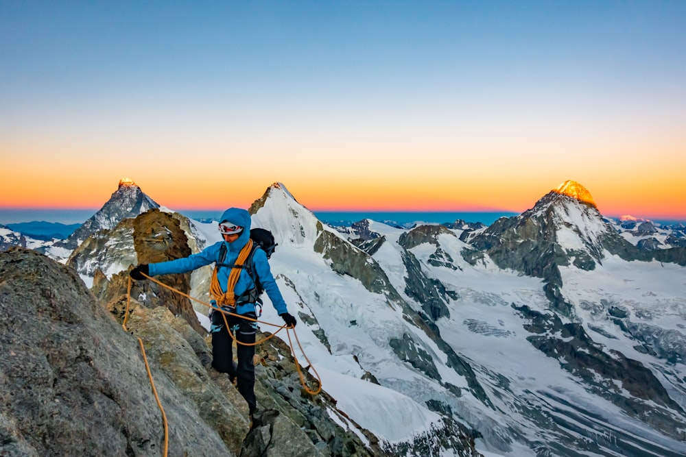 man in blue jacket and black pants standing on rock formation during daytime