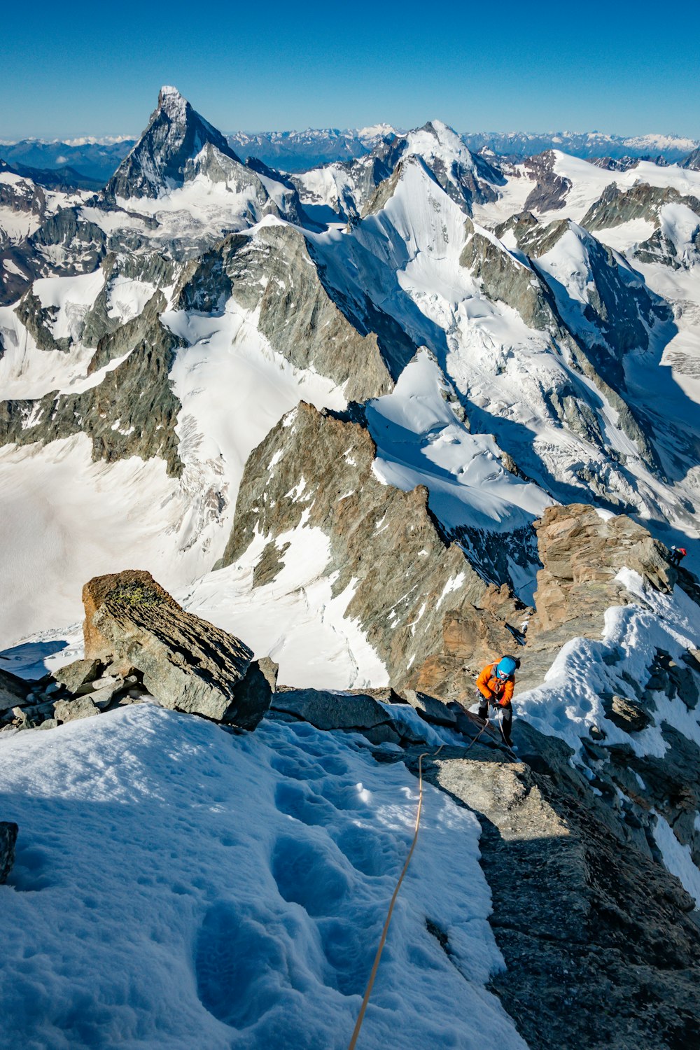 주황색 재킷과 검은 바지를 입은 사람이 낮에 눈 덮인 산에 서 있다