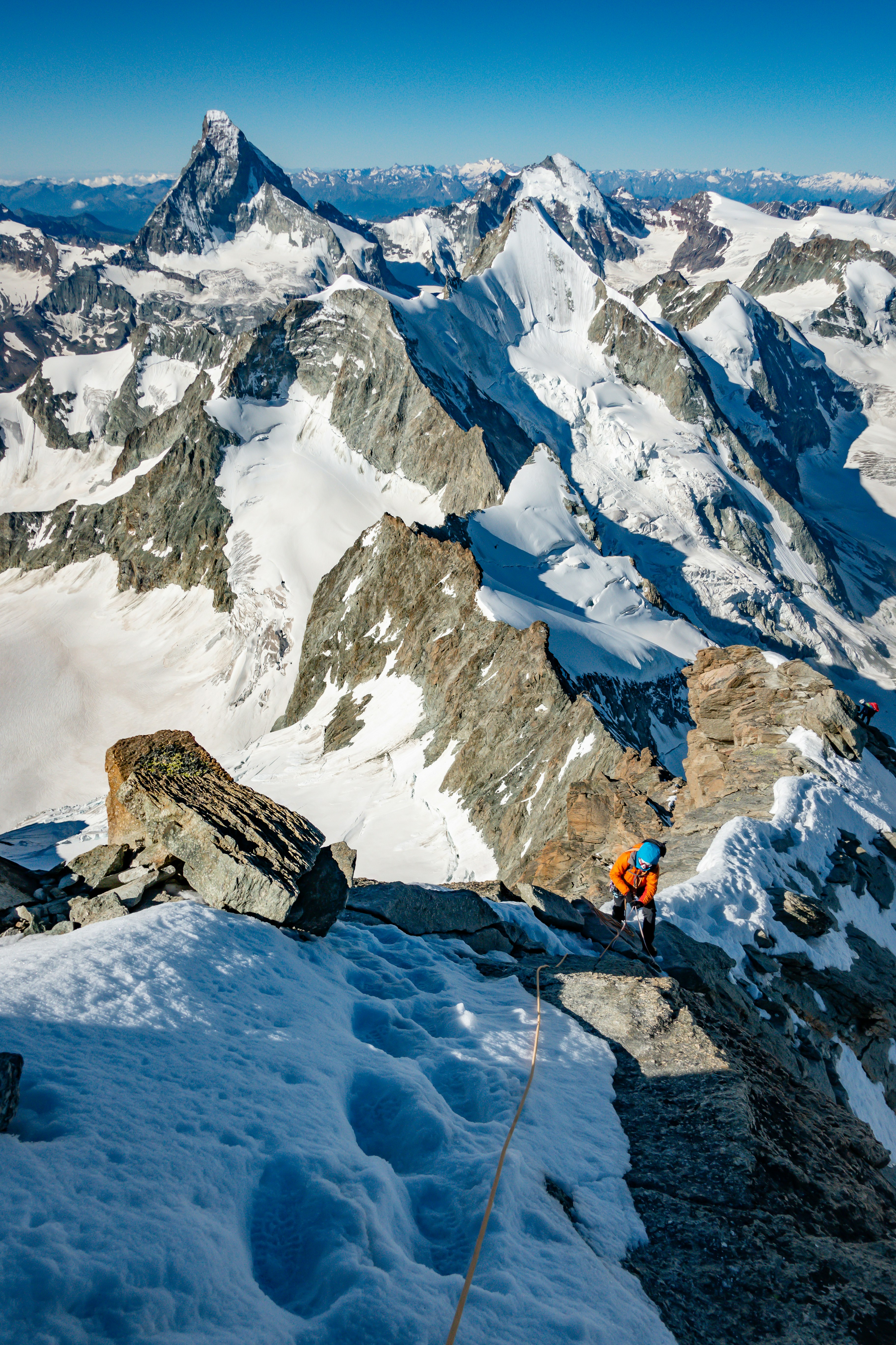 person in orange jacket and black pants standing on snow covered mountain during daytime