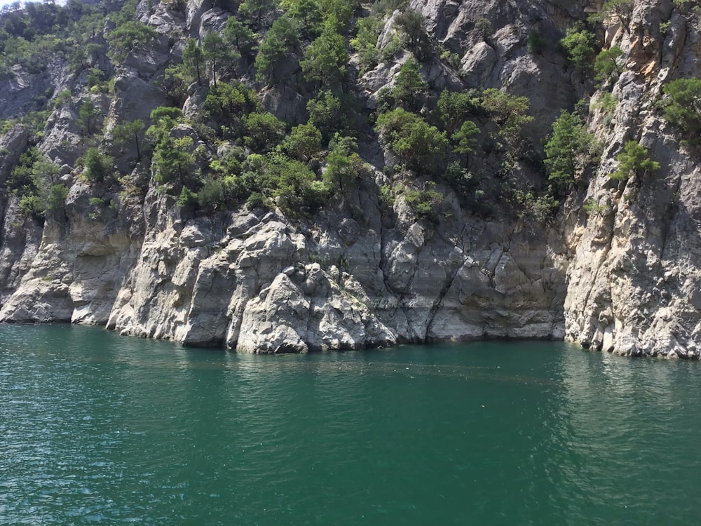 green body of water near gray rocky mountain during daytime