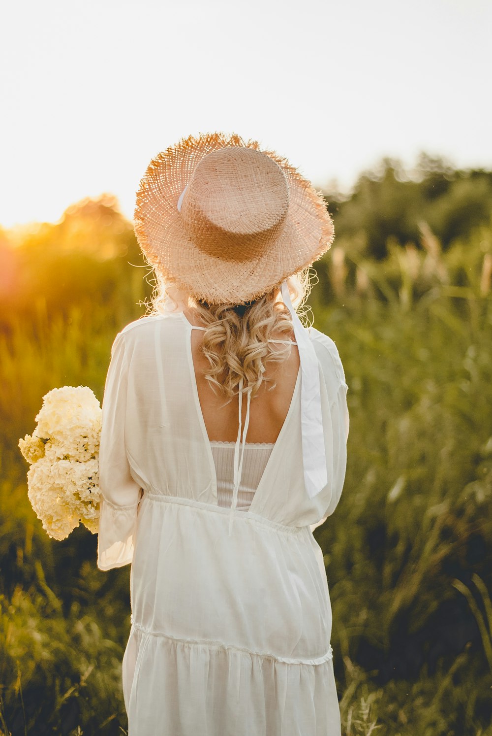 woman in white dress wearing brown sun hat standing on yellow flower field during daytime