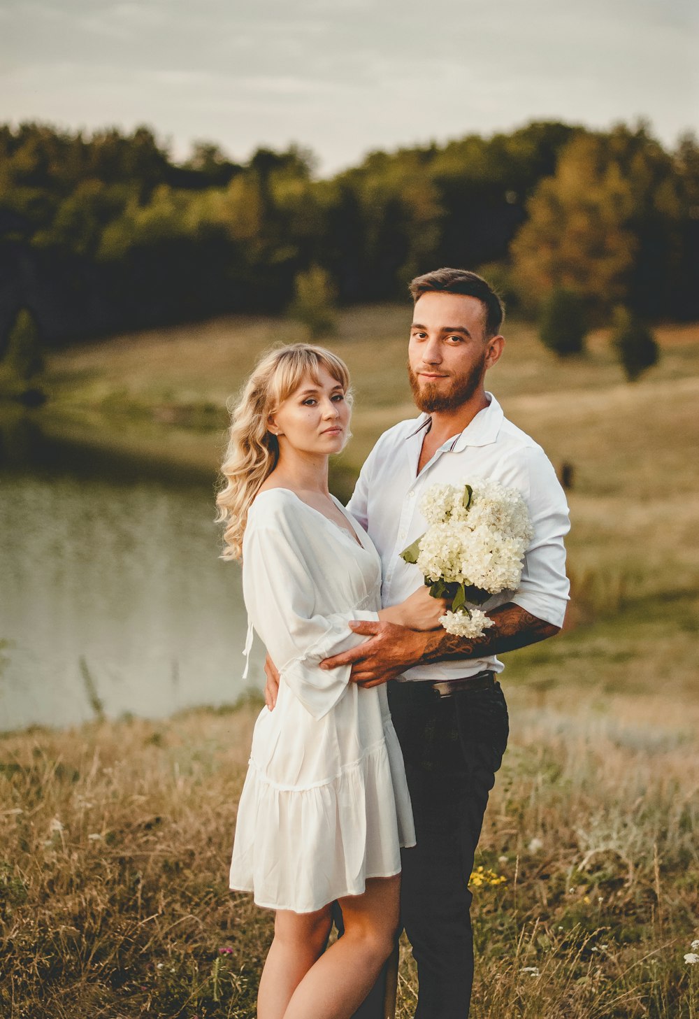 man in white dress shirt holding white flower bouquet beside woman in white dress