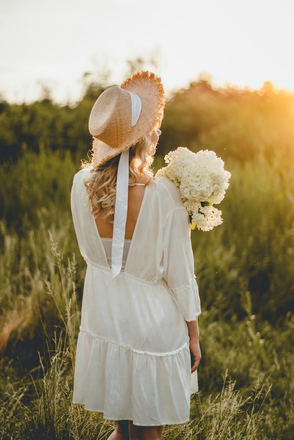 woman in white long sleeve dress wearing white sun hat standing on green grass field during