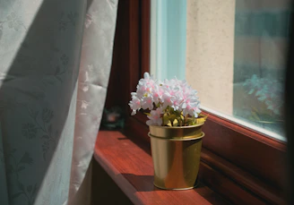 A handcrafted flowerpot holder painted in soft green tones, sitting by a sunlit window.