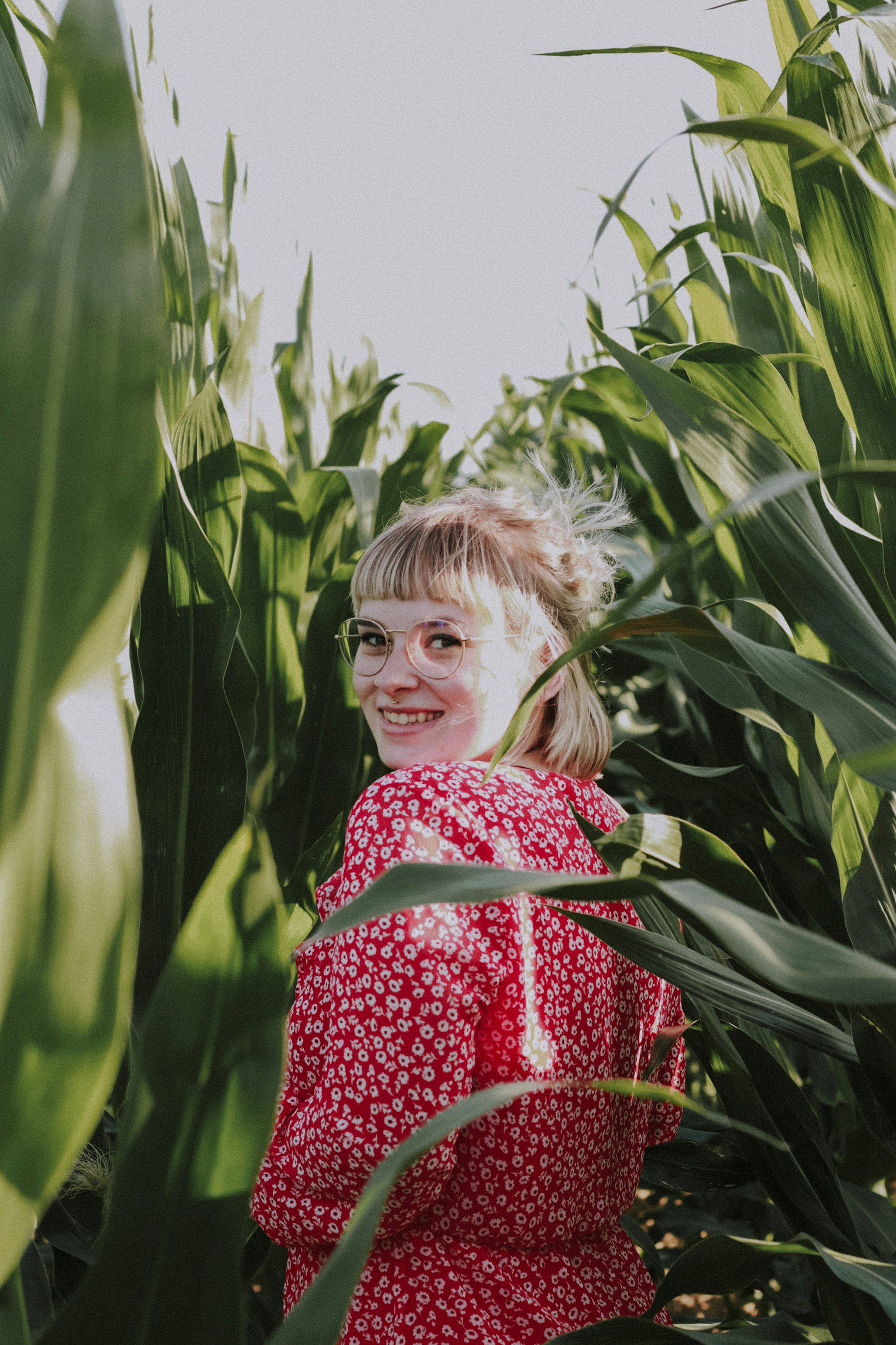 girl in red and white floral dress standing near green plant during daytime