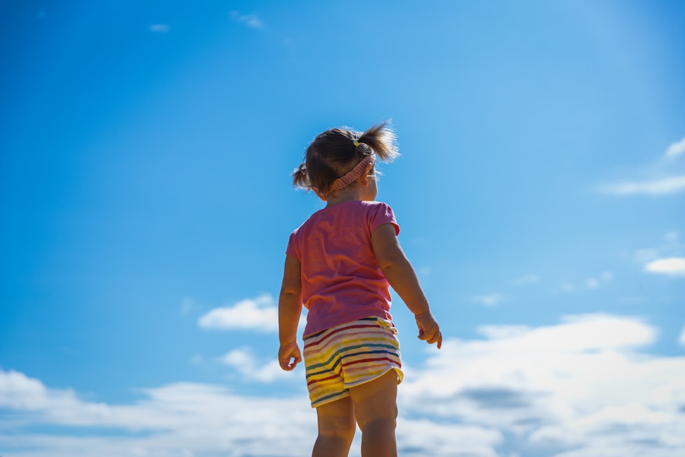 girl in pink t-shirt and yellow shorts standing on white clouds during daytime