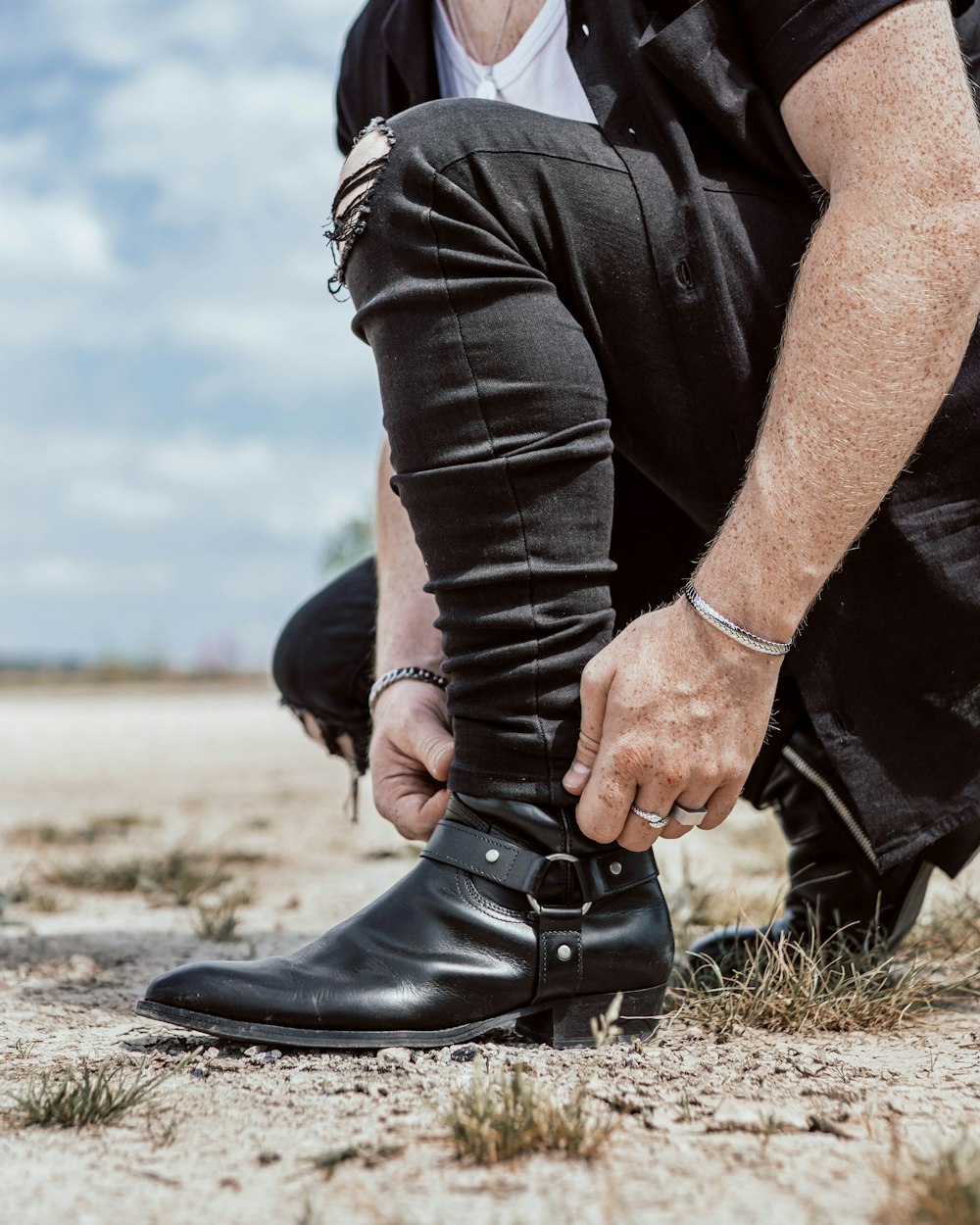 man in black leather jacket and black denim jeans sitting on ground during daytime