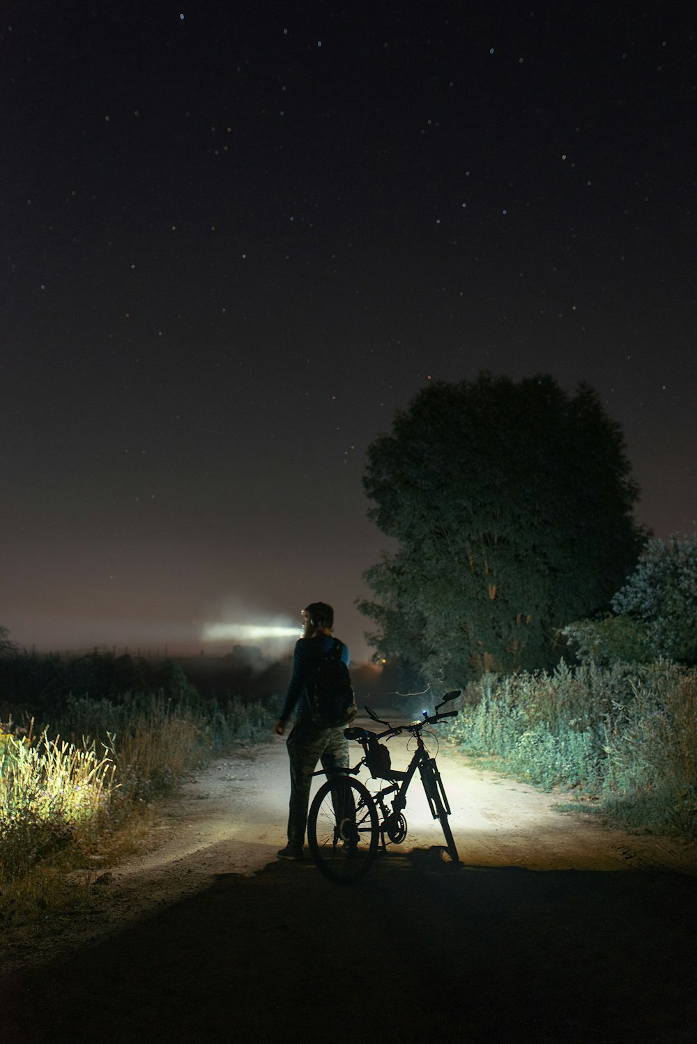man in black jacket riding bicycle on dirt road during night time