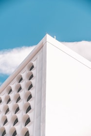 A modern architectural building with a triangular profile, featuring multiple arch-shaped windows. The structure is set against a clear blue sky with a few white clouds.